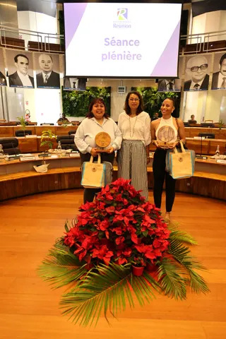 Deux lauréates avec leurs trophées et leurs cadeaux, accompagnées d’une invitée dans l’hémicycle.